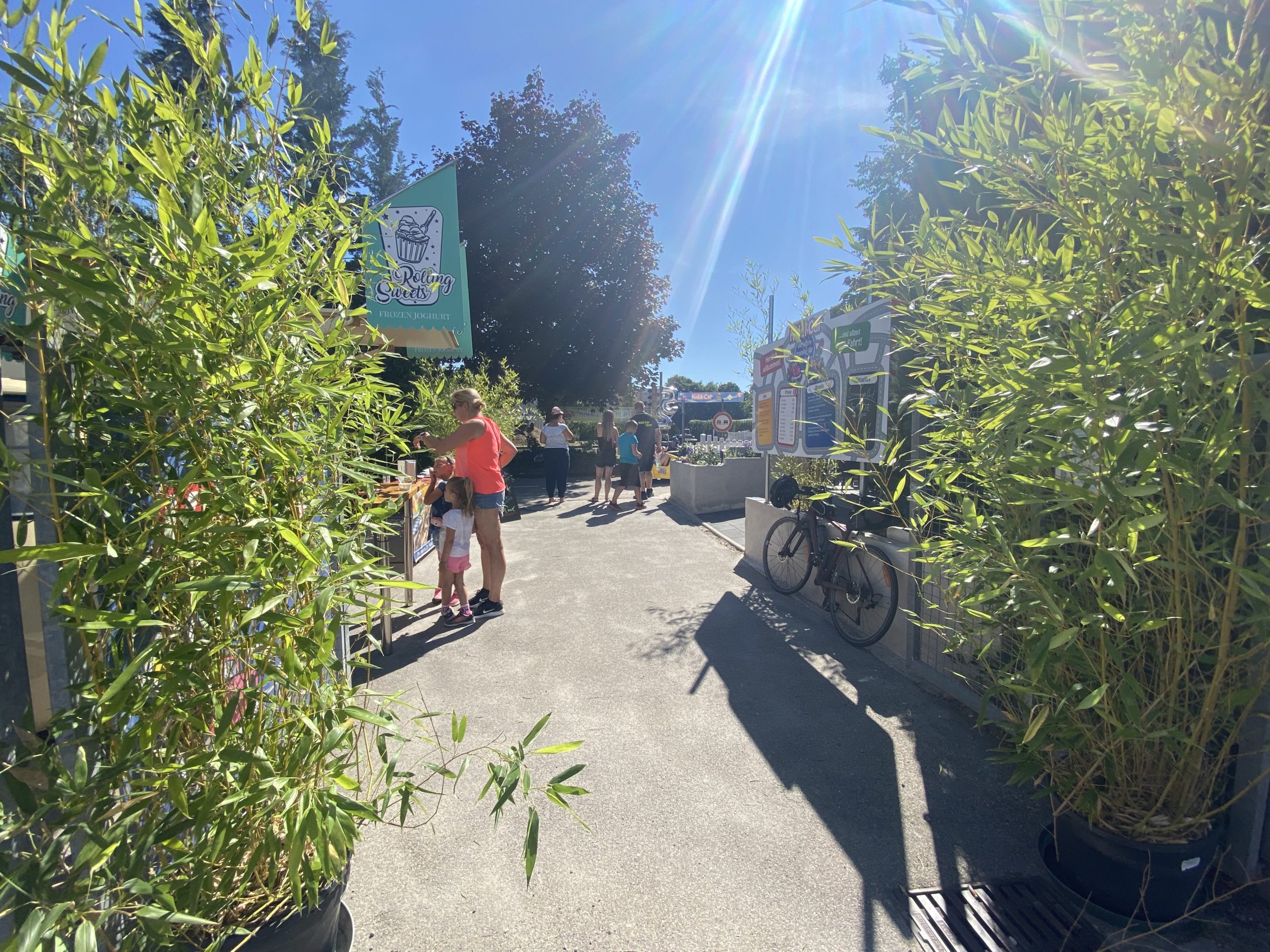 Muttertag in Fürstenfeldbruck: Verkehrsübungsplatz mit Kindern und Verkehrserzieher im Hintergrund. 2 Bambusse links und rechts umsäumen den Eingang vom Kiddi-Car Verkehrsübungsplatz in Fürstenfeldbruck