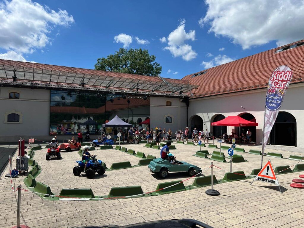 Übersicht über den Kiddi-Car Parcours beim KNAX-Fest 2025 im Kloster Fürstenfeld in Fürstenfeldbruck. Kinder fahren mit Elektroautos und Quads bei sommerlichen Temperaturen durch den Innenhof.