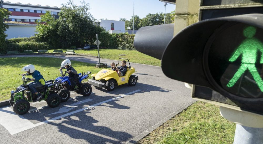 Grüne Fußgängerampel mit Kinderfahrzeugen im Hintergrund auf Verkehrsübungsplatz